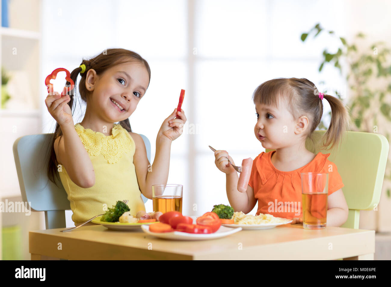 Cute children girls eating healthy food. Kids lunch at home, daycare center or kindergarten. Stock Photo