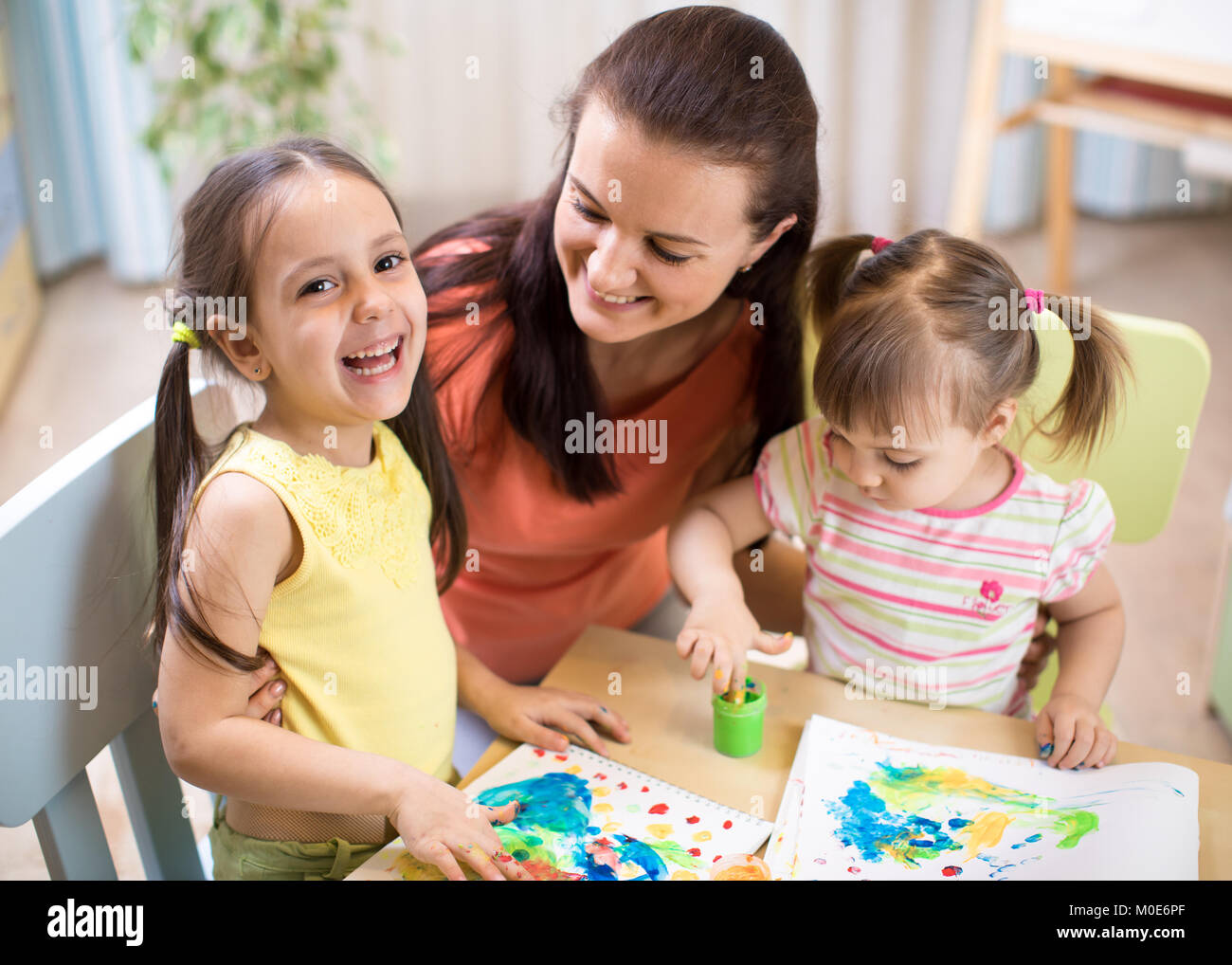 Mother and kids are painting together. Happy family are coloring with paintbrush. Woman and children have a fun pastime. Stock Photo