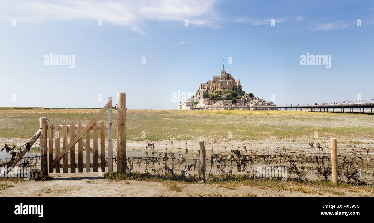 MONT SAINT MICHEL, NORMANDY, FRANCE - JUNE 26, 2017: Mont Saint Michel at low tide with green fields and a fence wicket in summer Stock Photo