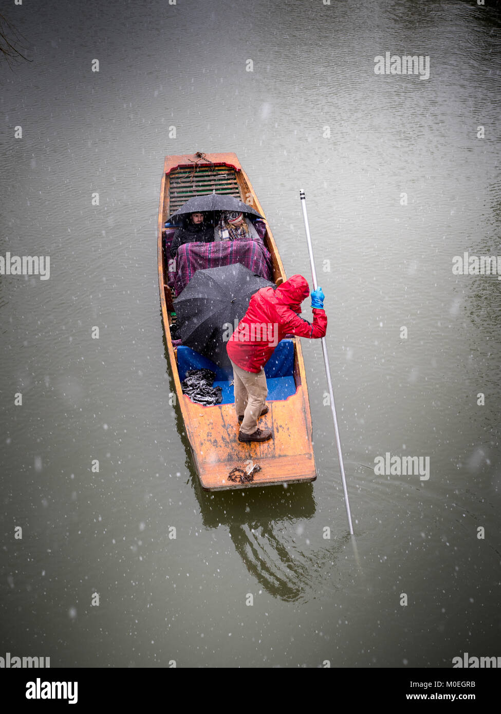 Winter Punting - Tourists huddle under blankets and umbrellas as they take a punt on the River Cam during snowy weather. Stock Photo