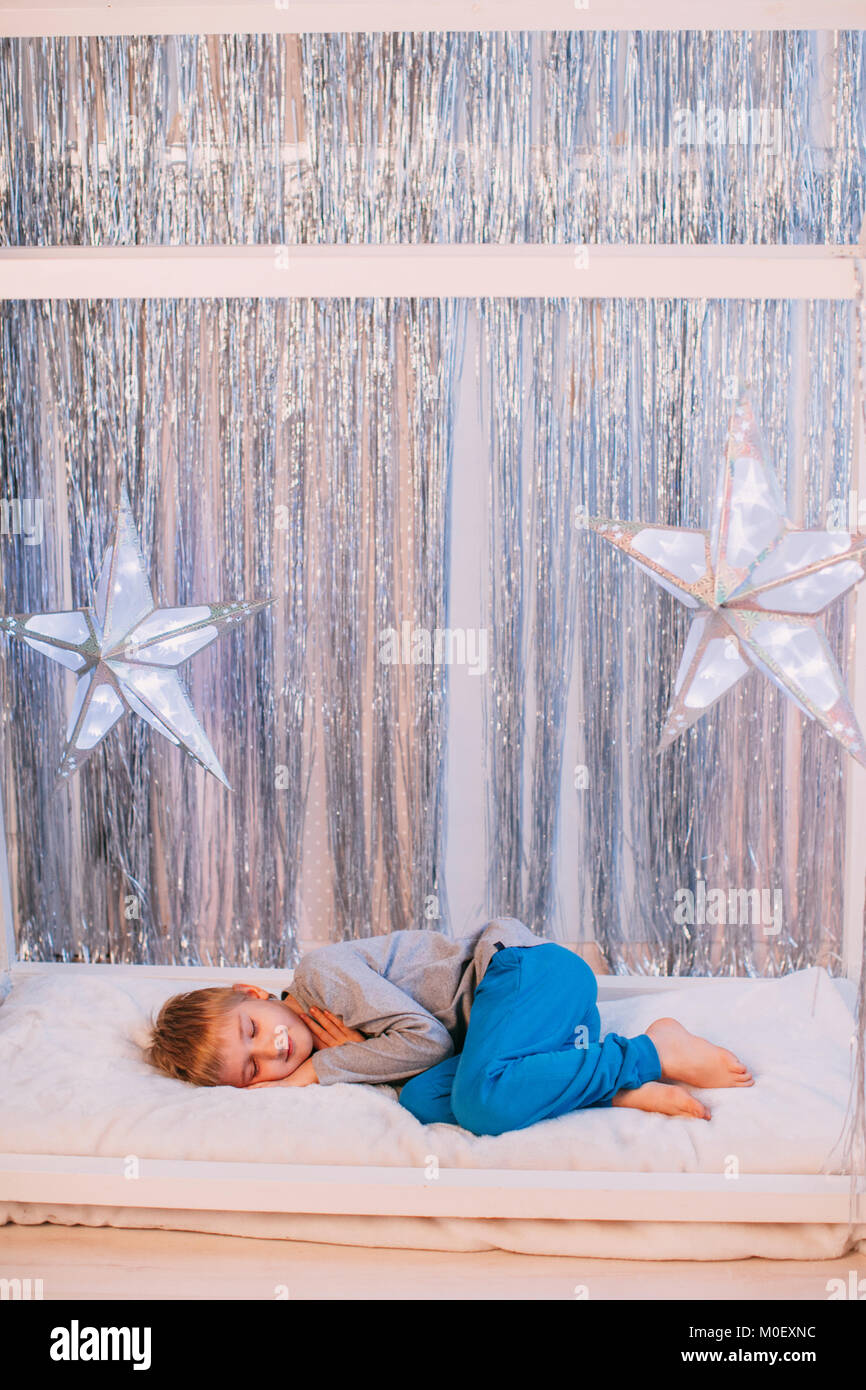 Boy curled up on a bed sleeping next to Christmas decorations Stock Photo