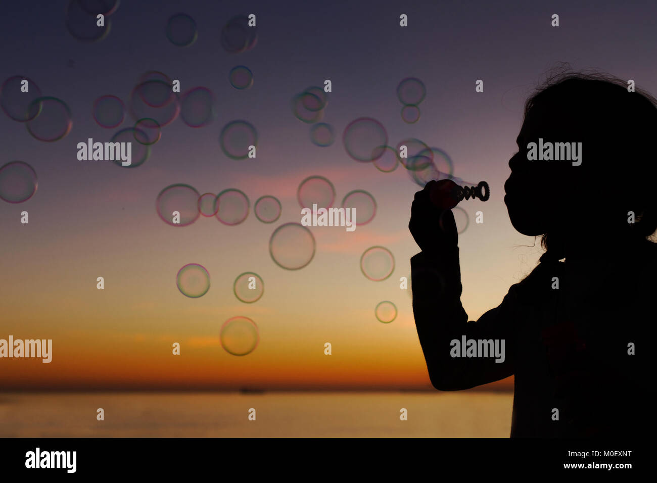 Silhouette of a girl holding a bubble wand blowing soap bubbles Stock Photo