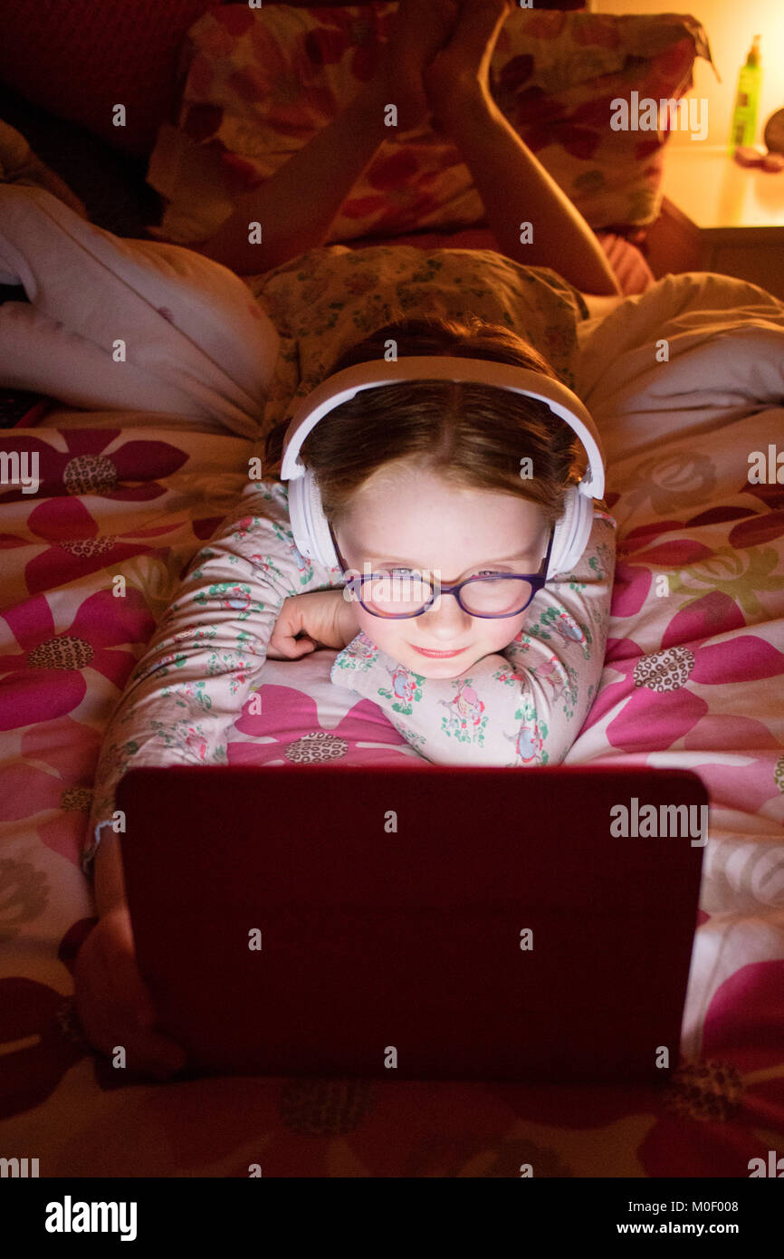 8 year old girl watching her ipad in her bedroom wearing headphones Stock Photo