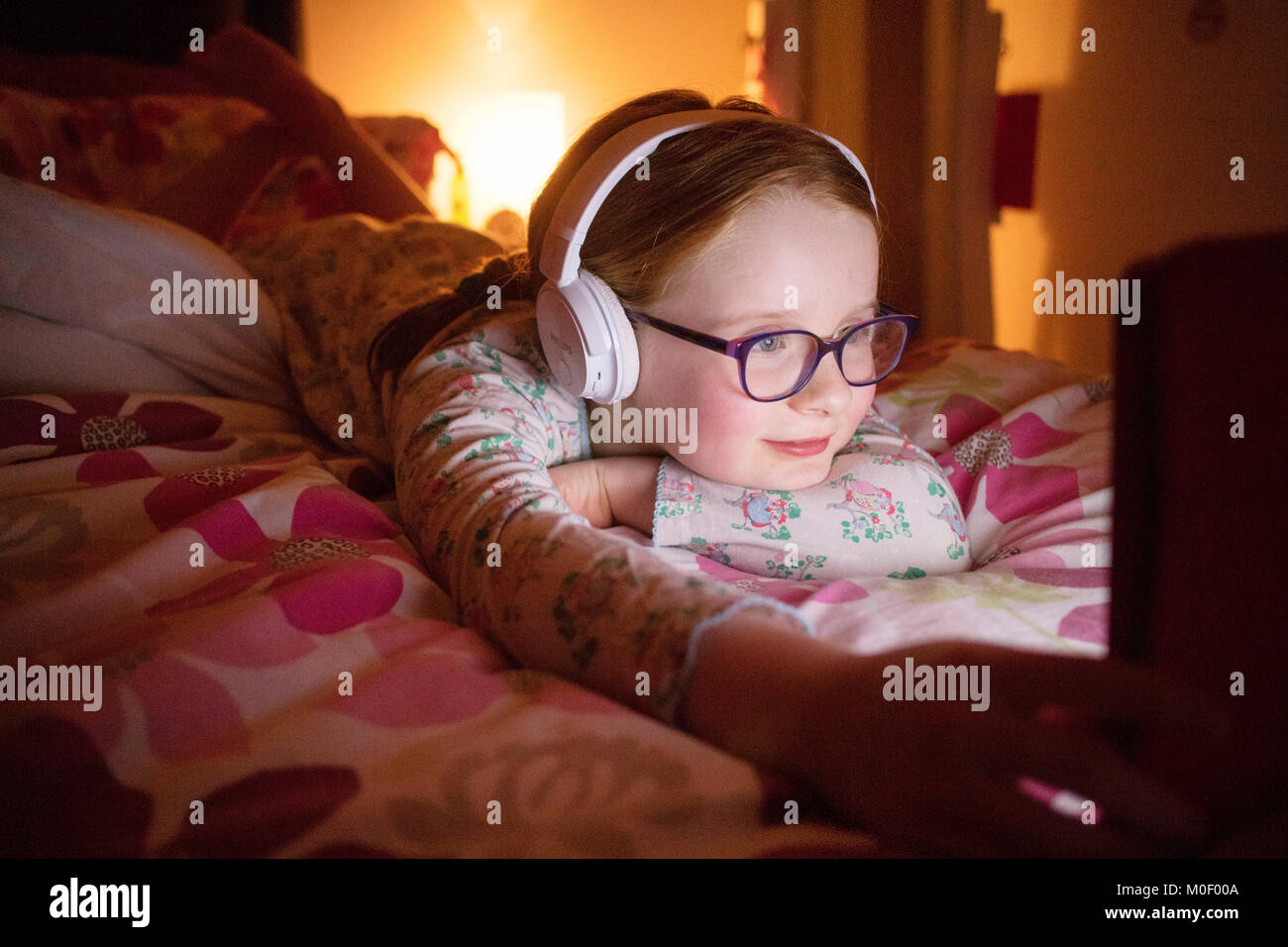 8 year old girl watching her ipad in her bedroom wearing headphones Stock Photo