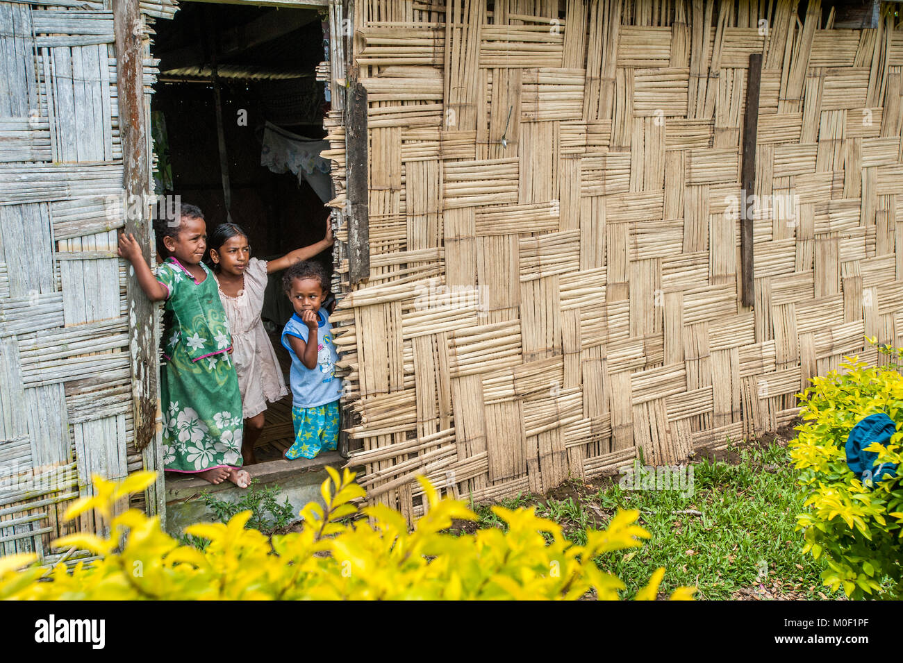 Three siblings look out the door of their home in a small remote village near Sigatoka on Viti Levu in the Fiji Islands. Stock Photo