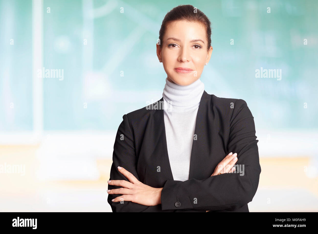 A Lovely Female Teacher Standing With Arms Crossed In Front Of The Chalkboard In The Classroom 