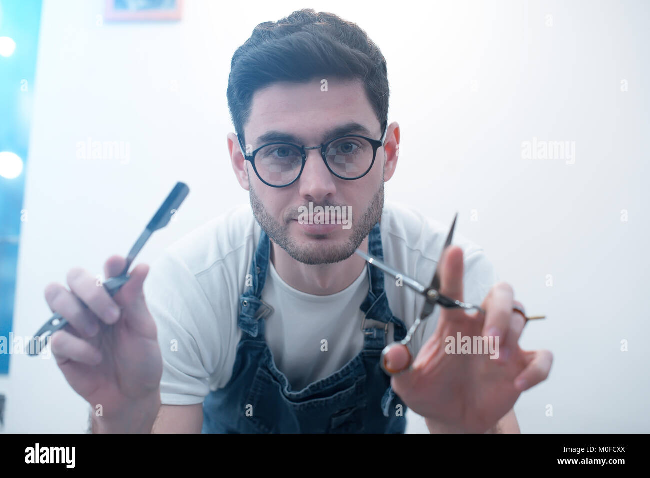 Barber keeps scissors and a razor against the background of a white wall. Stock Photo