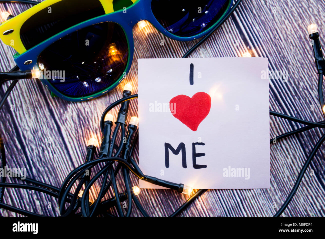 I love me on Sticky note with sunglasses, wooden background with lights