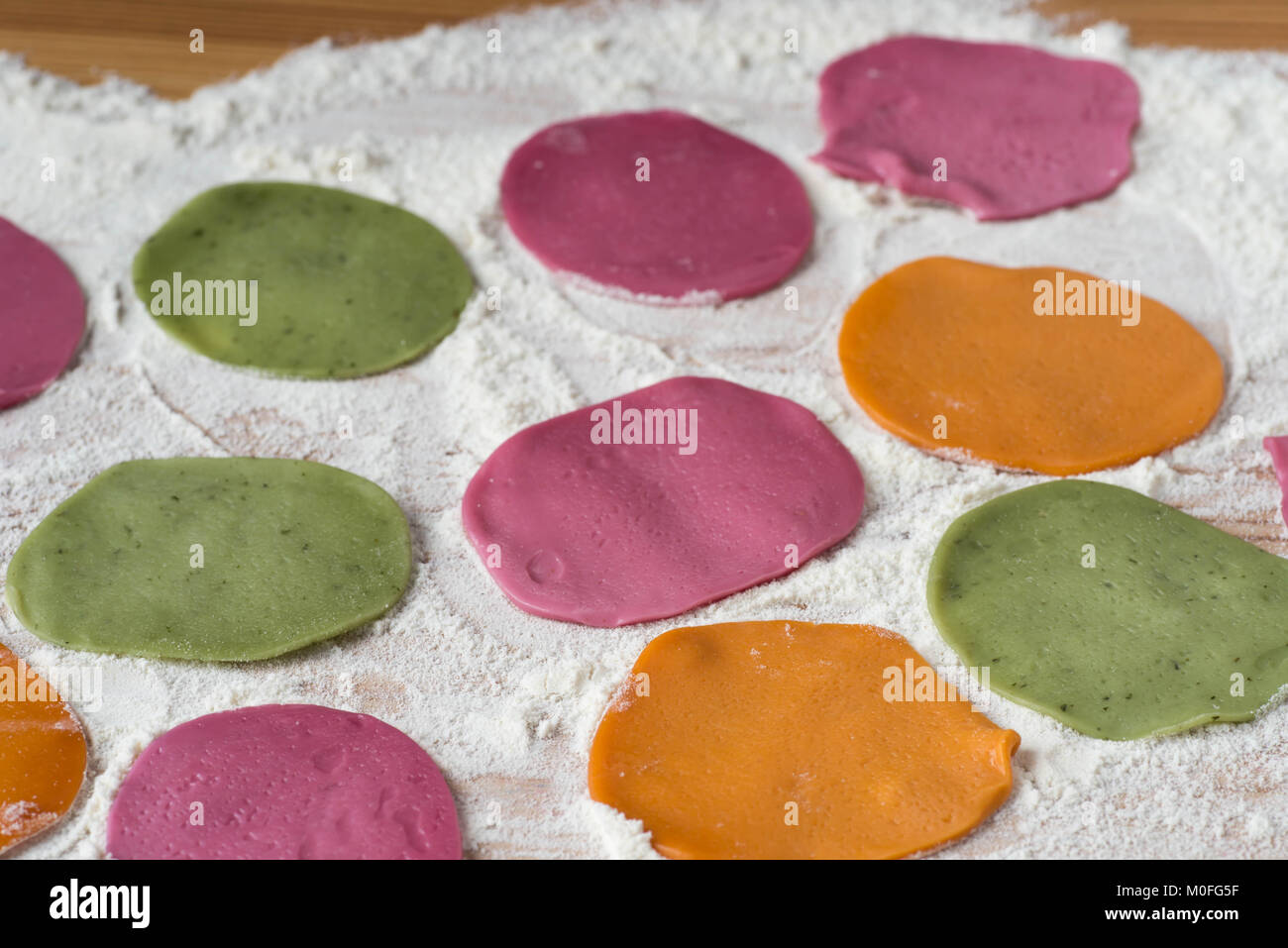 multicolored dyed pieces of raw dough for dumplings on table Stock Photo