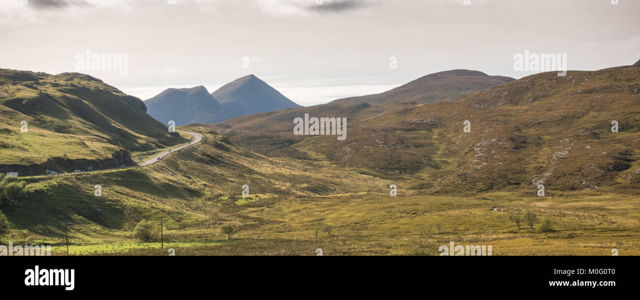 The A835 road, part of the North Coast 500 touring route, winds past Knockan Crag at Elphin in Assynt, with Cul Beag mountain rising behind. Stock Photo