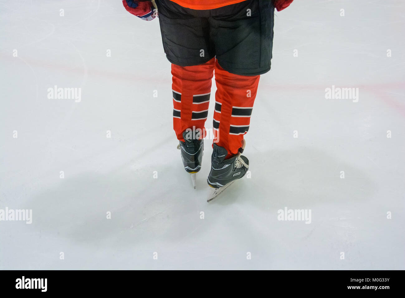 Closeup image of hockey player's legs and feet in red and black uniform