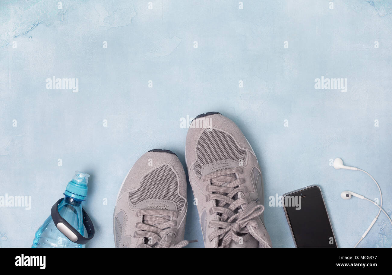 gray sneakers, water bottle, fitness bracelet, smartphone with headphones on a blue background. view from above Stock Photo