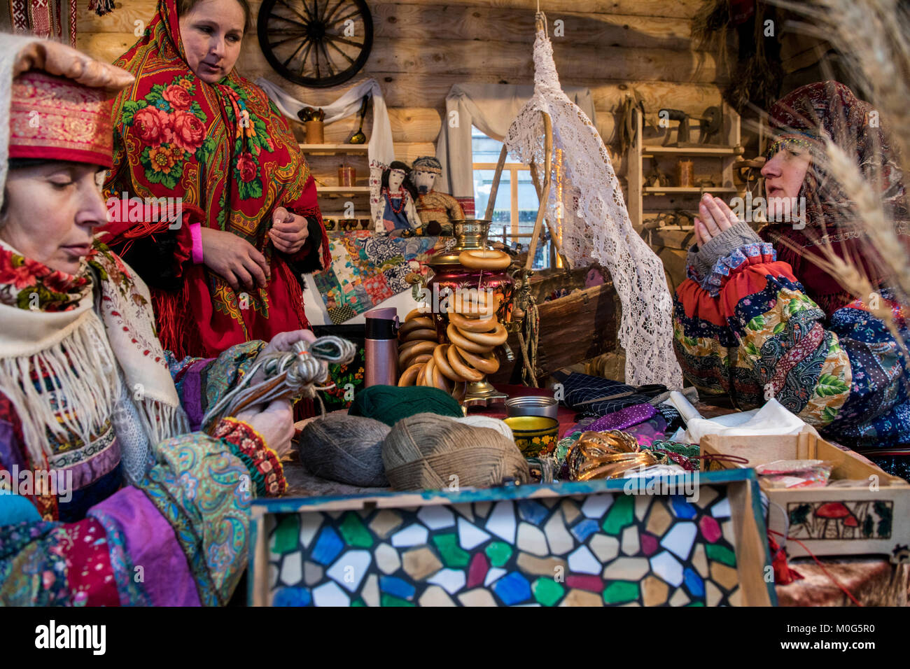 Women in Russian national costumes do needlework in a traditional russian house at a table with a samovar and bagels, Russia Stock Photo