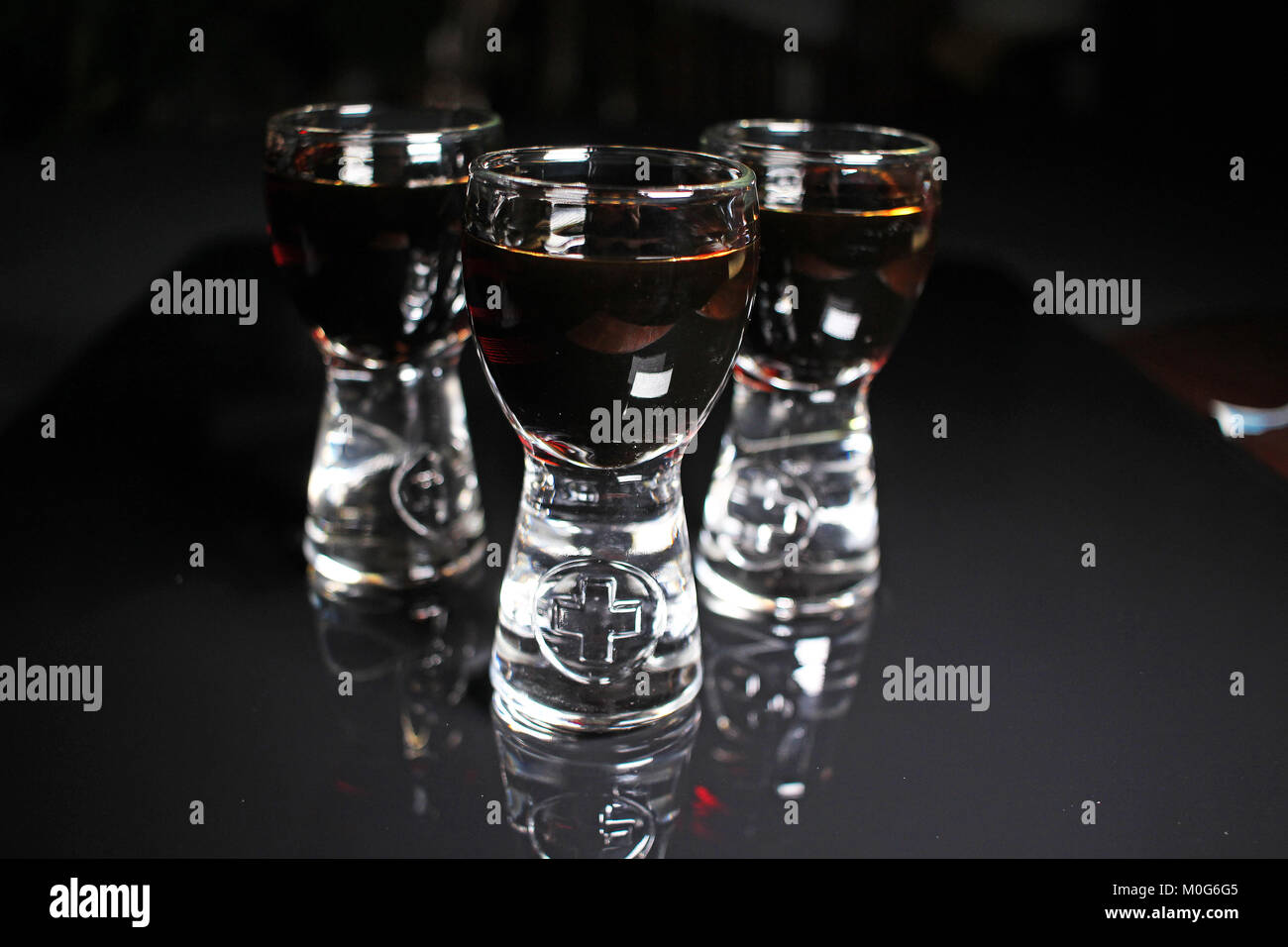 Rum shots. Alcohol shot brown dark rum on black reflective studio