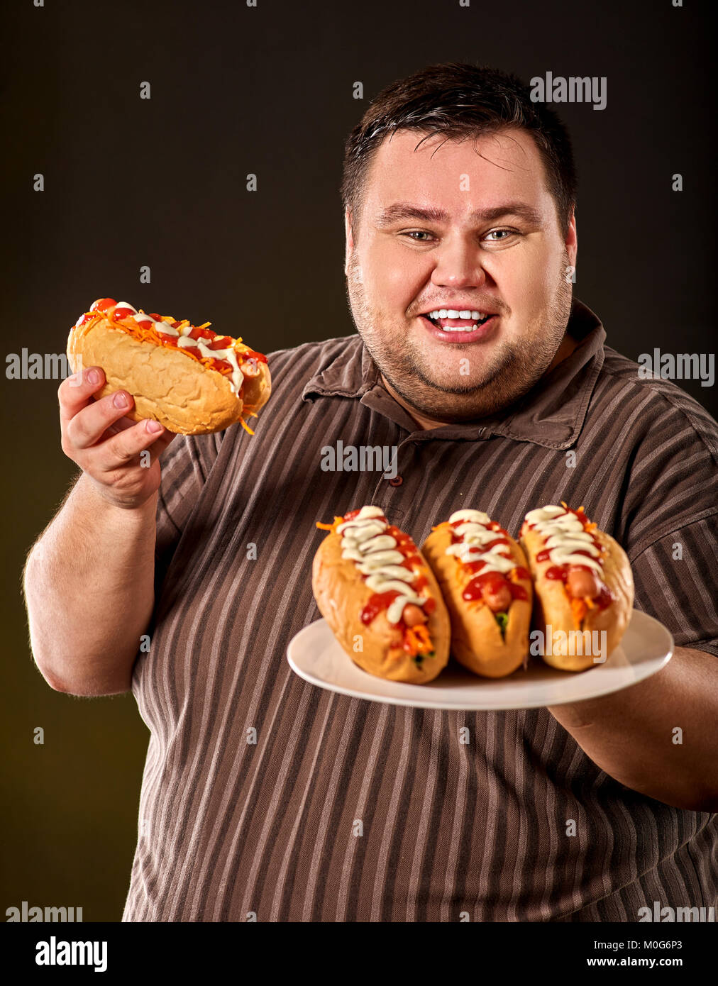 Fat man eating fast food hot dog. Breakfast for overweight person. Stock Photo
