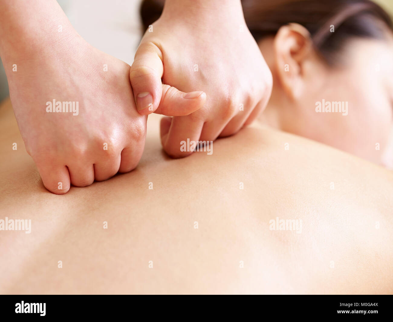 close-up of hands of a masseur massaging back of a young asian woman Stock Photo