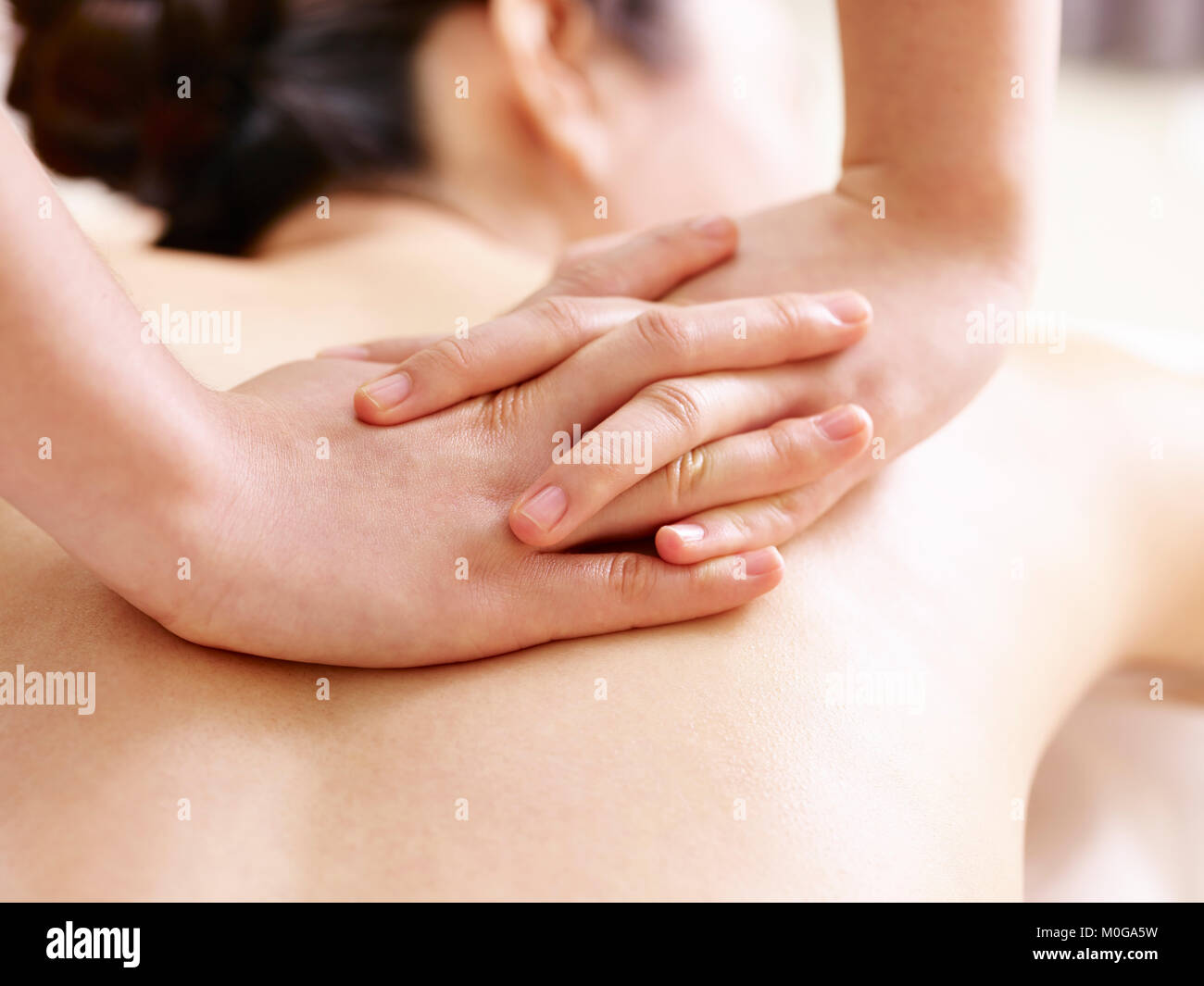 close-up of hands of a masseur massaging back of a young asian woman Stock Photo