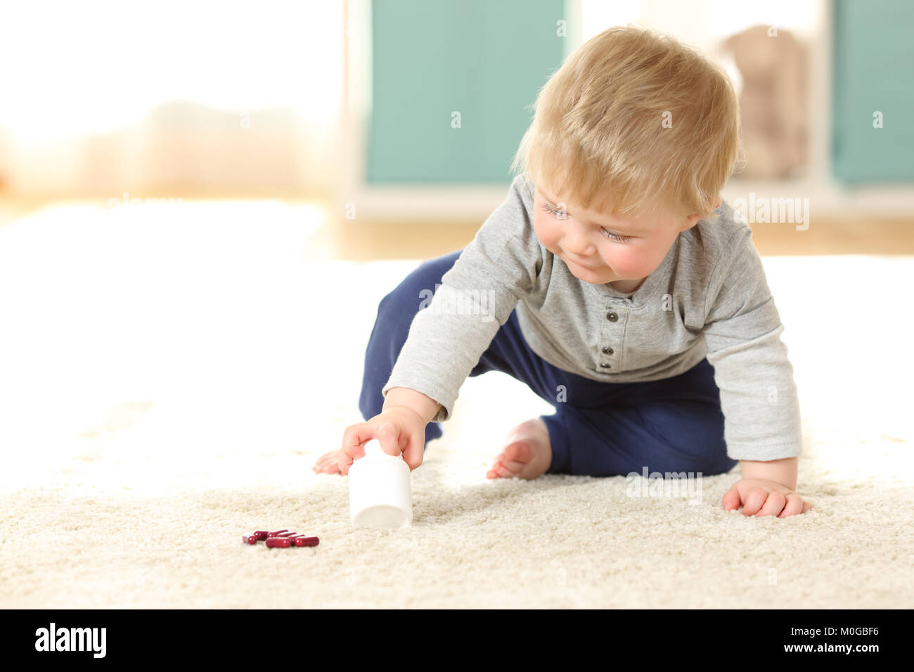 Baby in danger playing with a bottle of pills on the floor at home Stock Photo