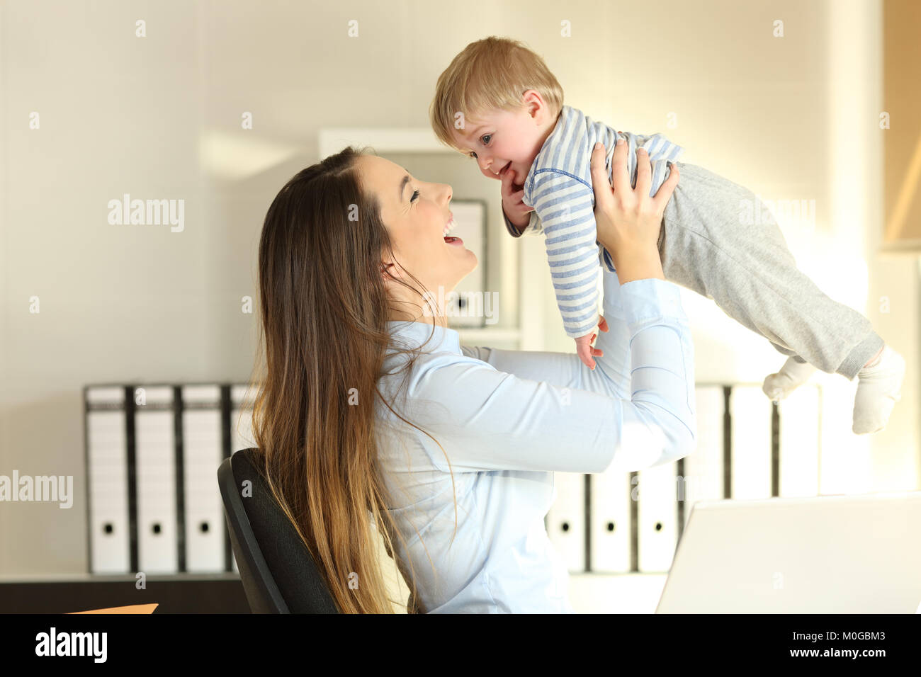 Side view portrait of a happy working mother raising her baby son at office Stock Photo
