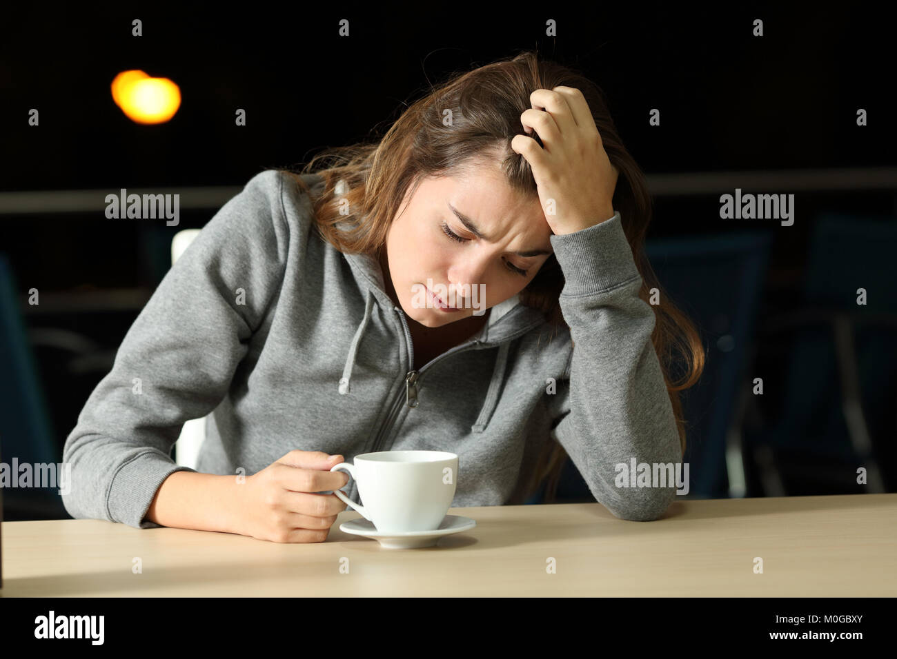 Portrait of a sad teen complaining alone in a coffee shop in the night Stock Photo