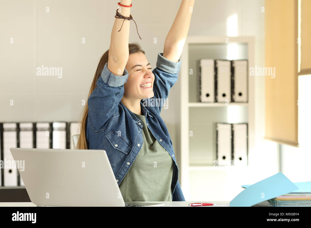 Portrait of a young satisfied intern raising arms at office Stock Photo