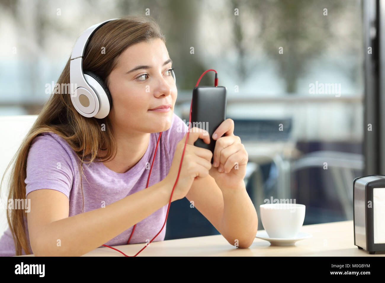 Single teen wearing headphones listening to music from a smart phone in a coffee shop terrace Stock Photo
