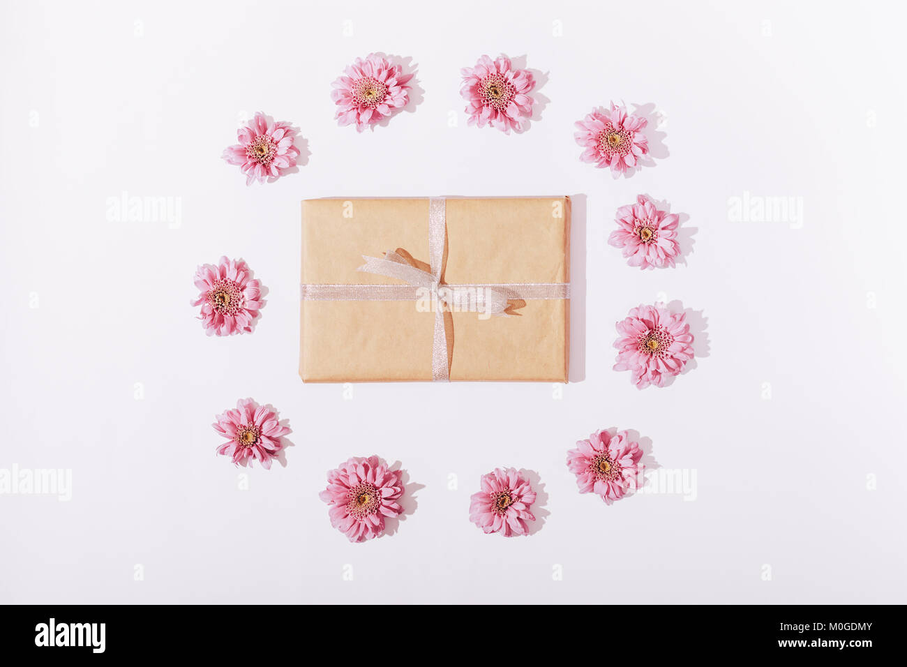 Gift box in wrapping paper with a bow and pink flowers on a white ...