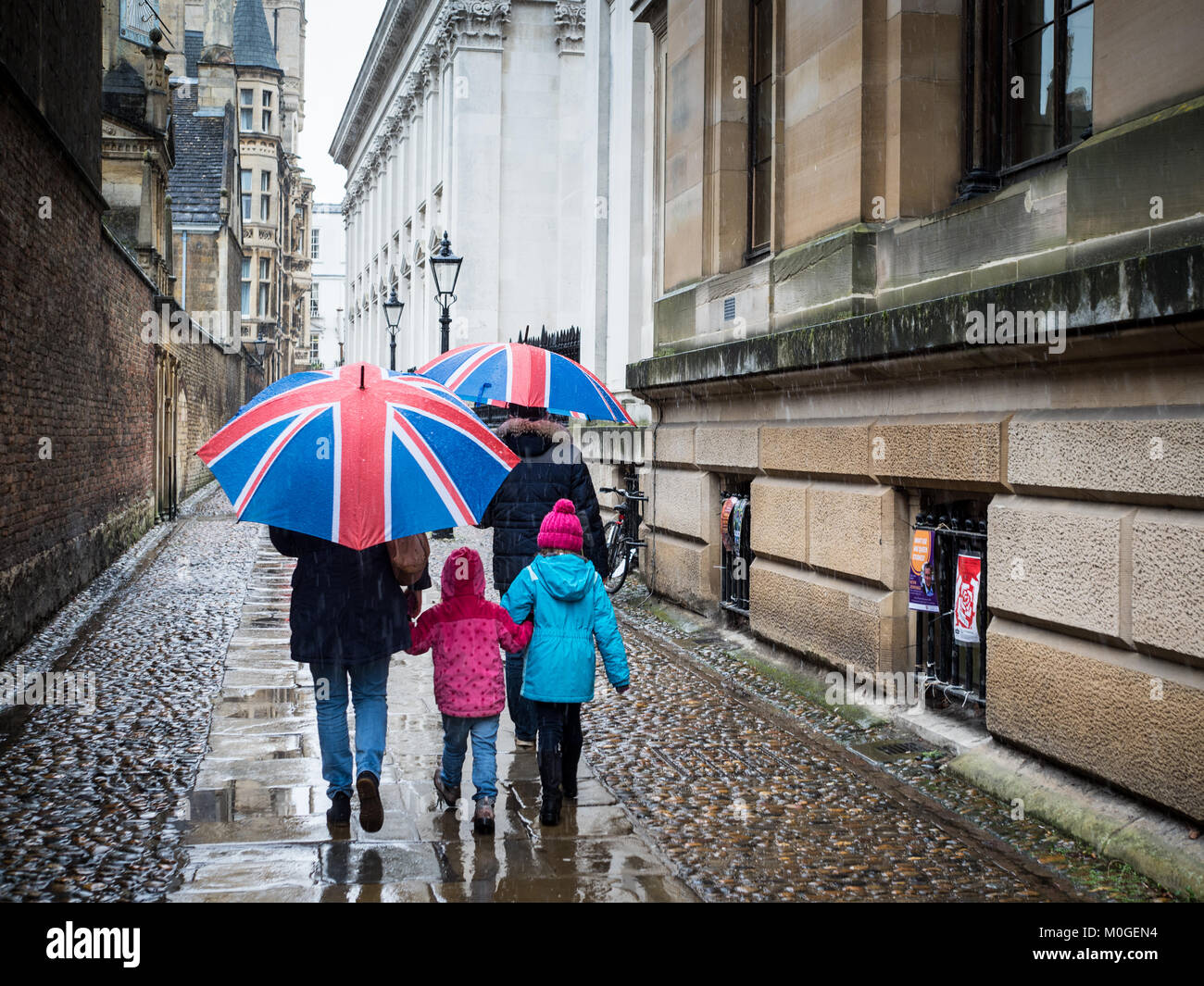 Cambridge Tourism - a family walk through the historic centre of Cambridge on a rainy day with Union Jack umbrellas Stock Photo