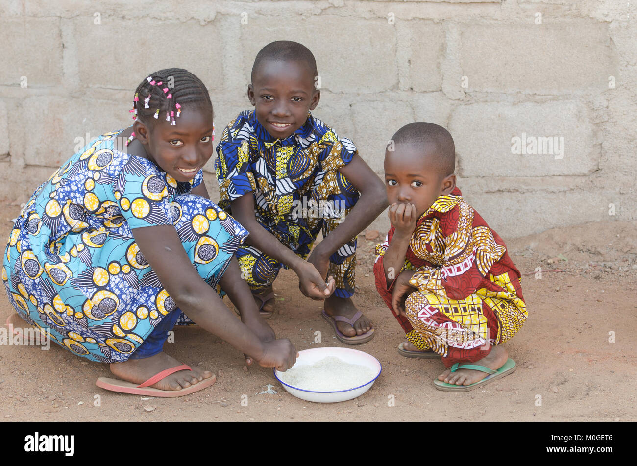 Three African Children Sitting Outdoors Eating Rice in Africa Stock Photo