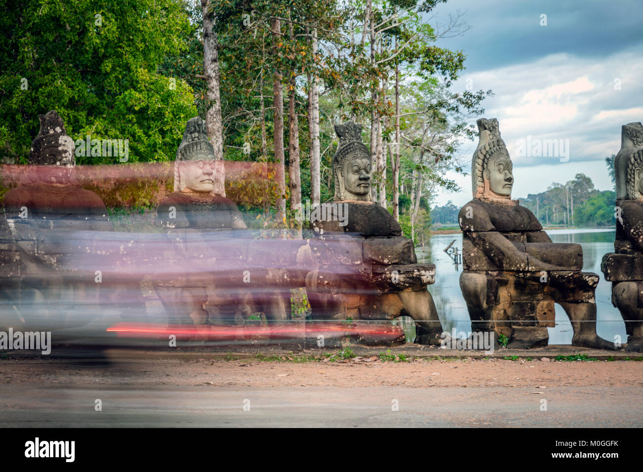 Tuk tuk passing statues on bridge at South Gate Bayon Temple, Angkor Thom, Cambodia. Stock Photo