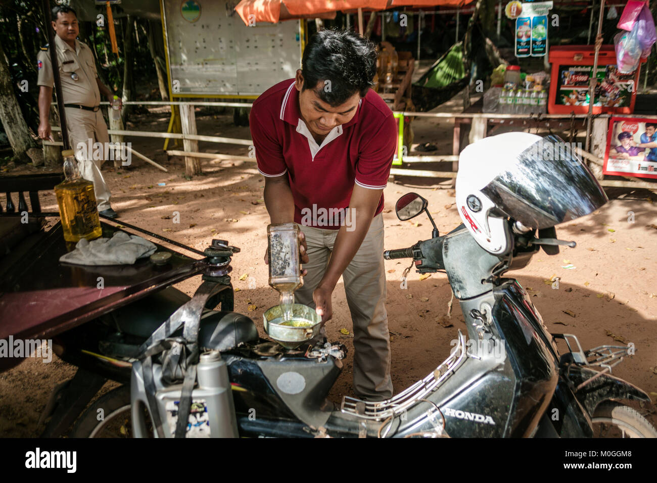 Tuk tuk driver filling tank with fuel from old bourbon whiskey bottle, Angkor Thom, Cambodia. Stock Photo