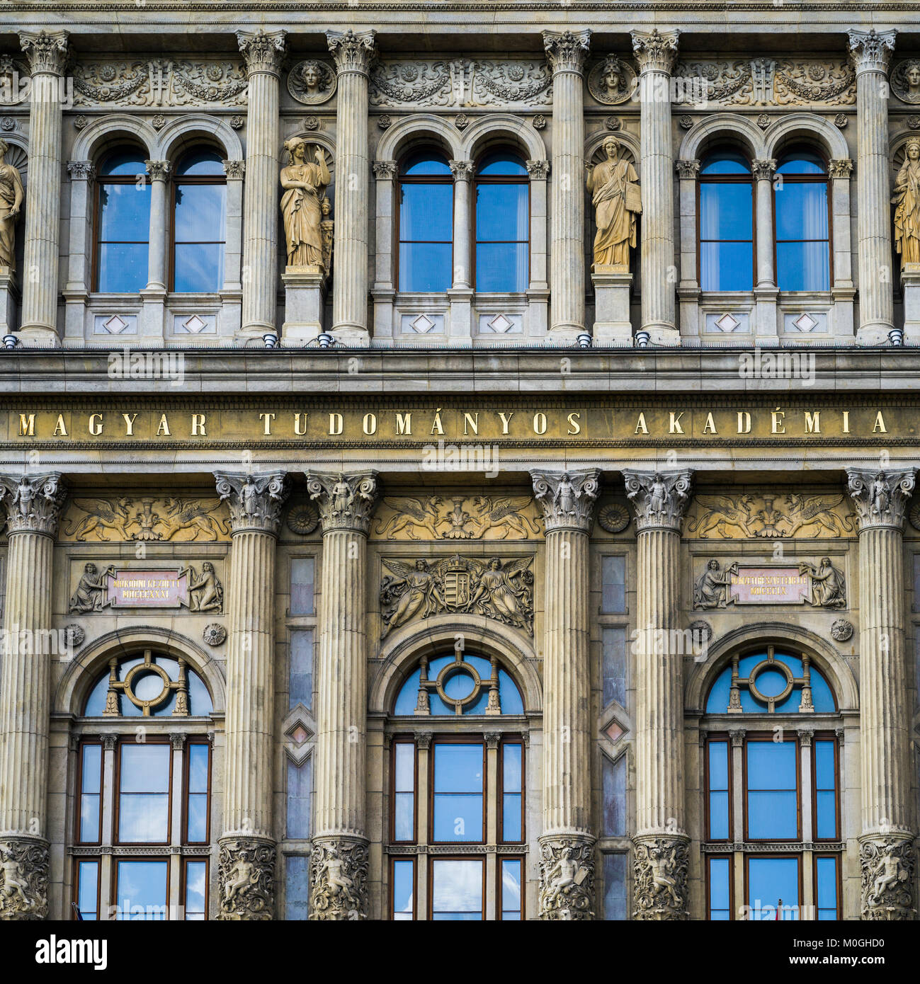 Ornate facade of a building with pillars and statues beside windows with reflection of the blue sky; Budapest, Budapest, Hungary Stock Photo
