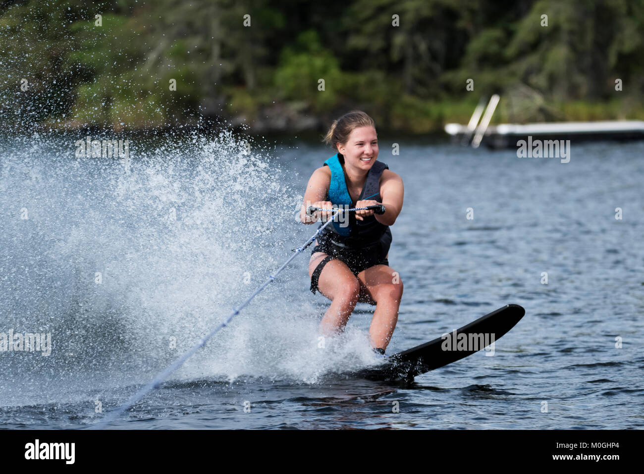 A young woman wakeboarding behind a boat on a lake; Lake of the Woods, Ontario, Canada Stock Photo