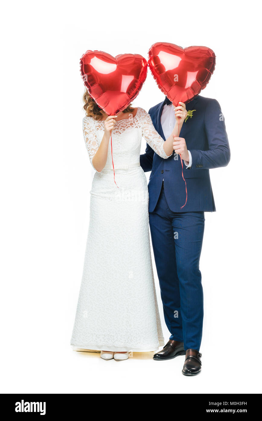 wedding couple covering faces with red heart shaped balloons isolated