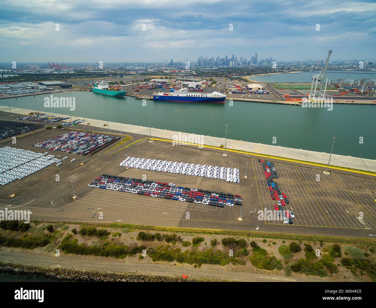 Aerial view of Port Melbourne with moored cargo vessels, imported cars parking lots, and Melbourne CBD skyline on the horizon Stock Photo