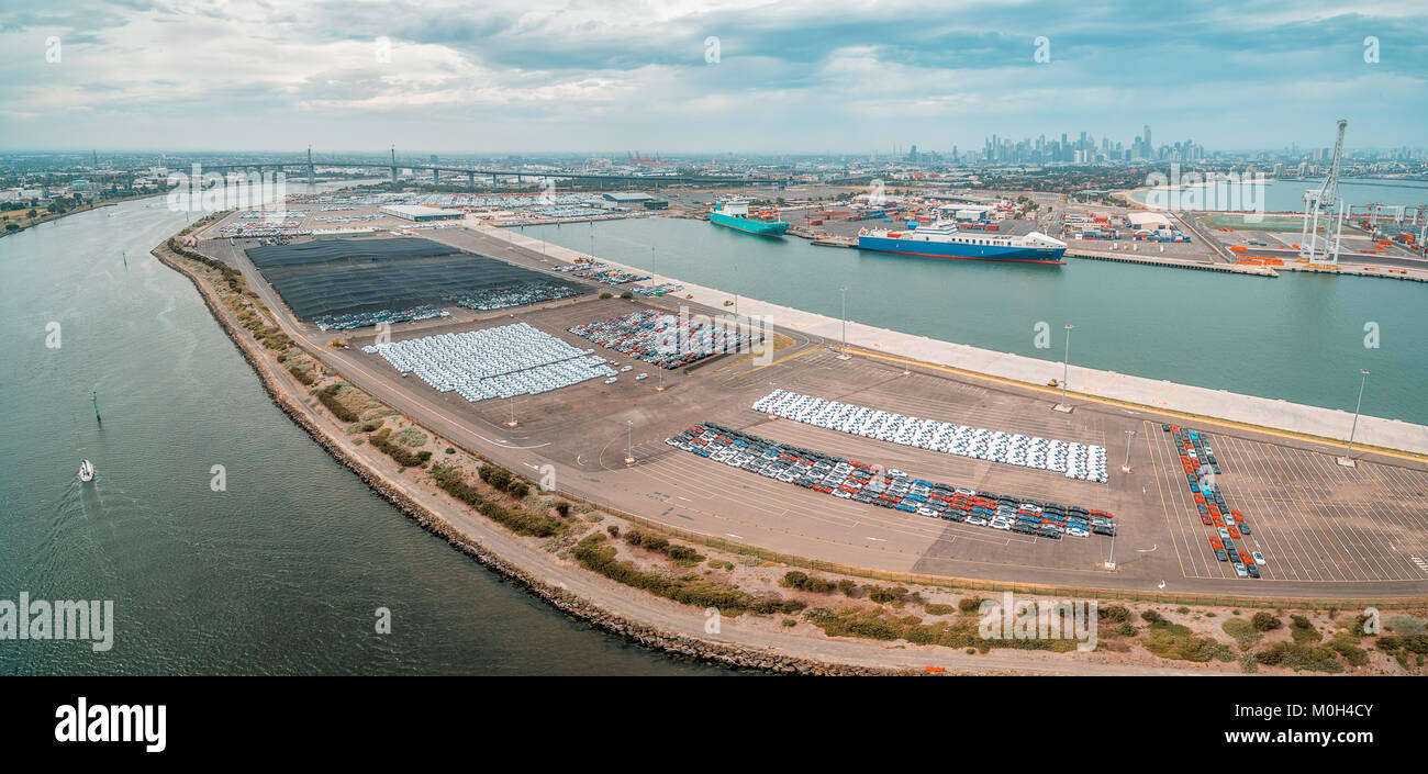 Aerial panorama of Port Melbourne with moored cargo vessels, imported cars parking lots, and Melbourne CBD skyline on the horizon Stock Photo