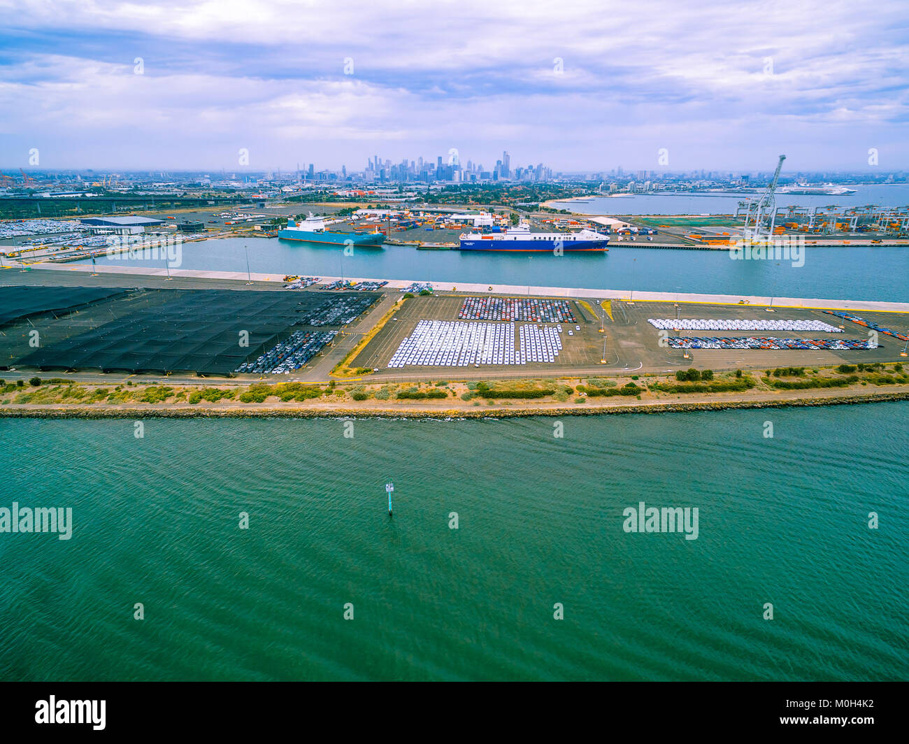 Aerial view of Port Melbourne with moored cargo vessels, imported cars parking lots, and Melbourne CBD skyline on the horizon Stock Photo