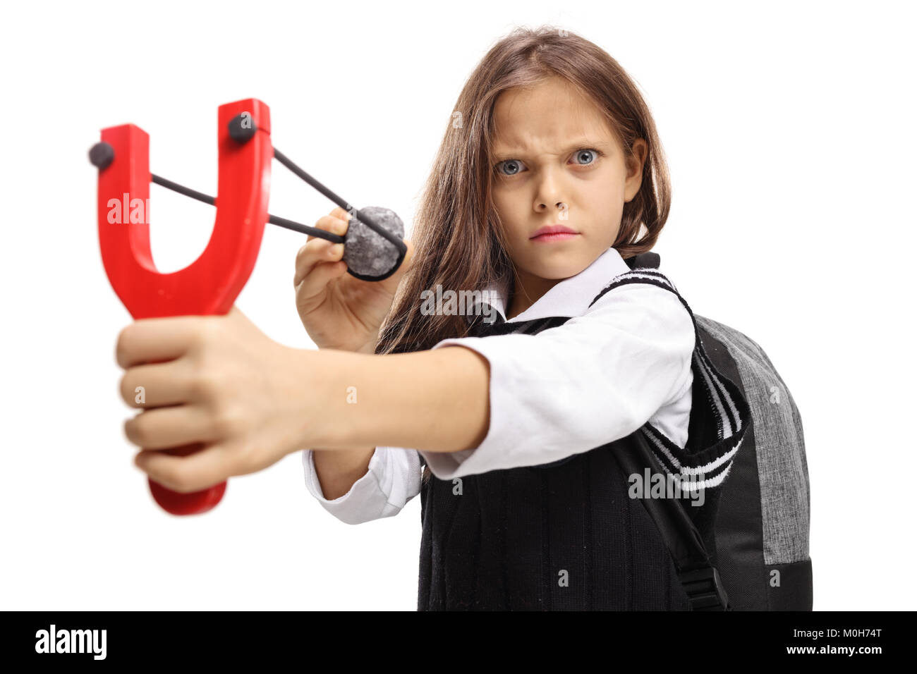 Angry little schoolgirl aiming with a stone and a slingshot isolated on white background Stock Photo