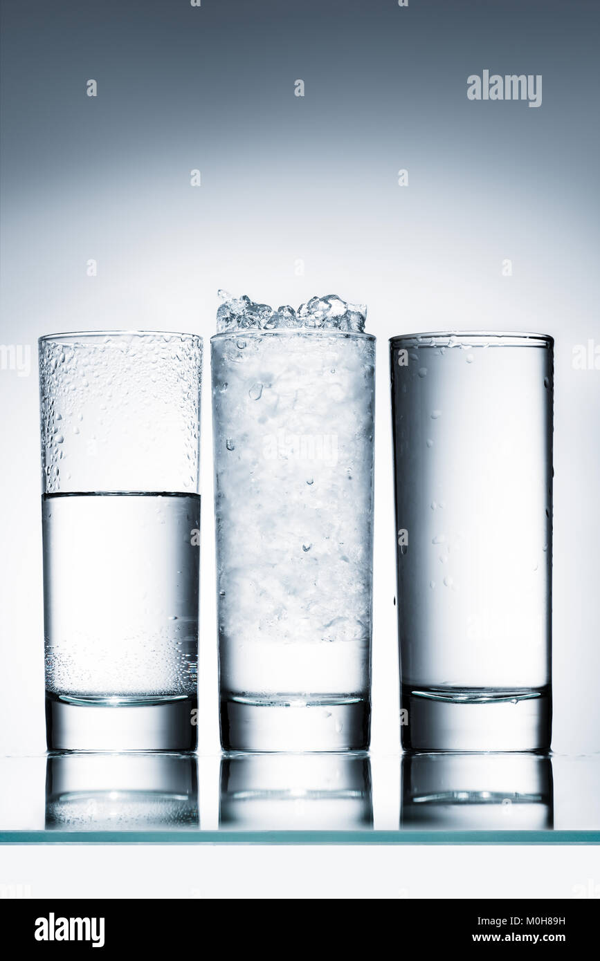 glasses of water in row and one with ice on reflective surface Stock ...