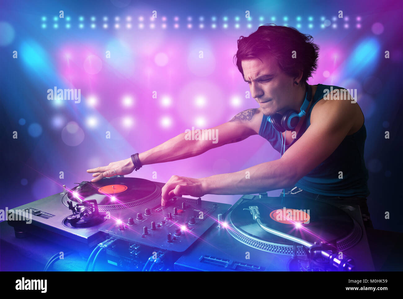 Young disc jockey mixing music on turntables on stage with lights and