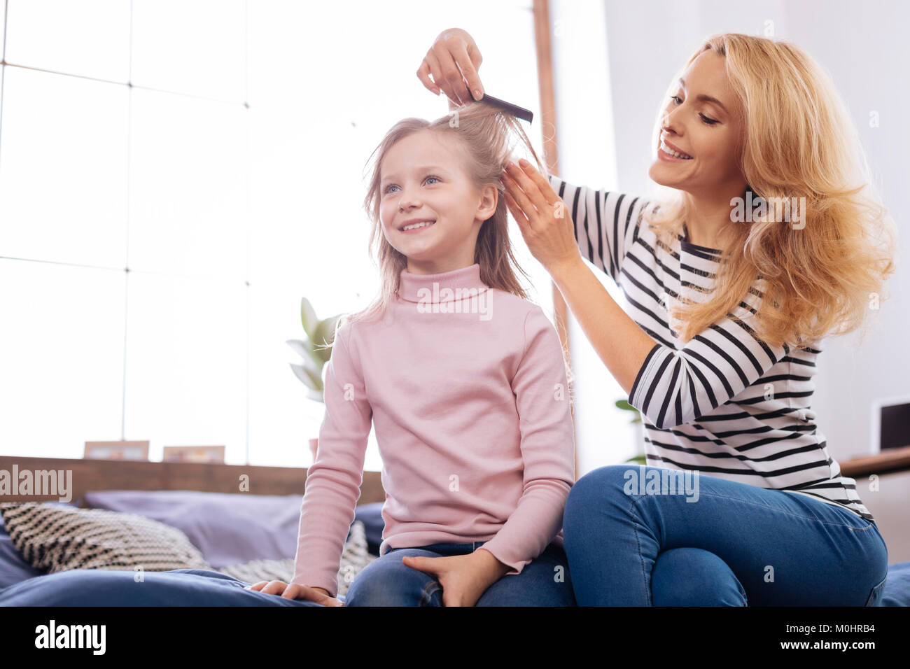 Cheerful mother combing her daughters hair Stock Photo
