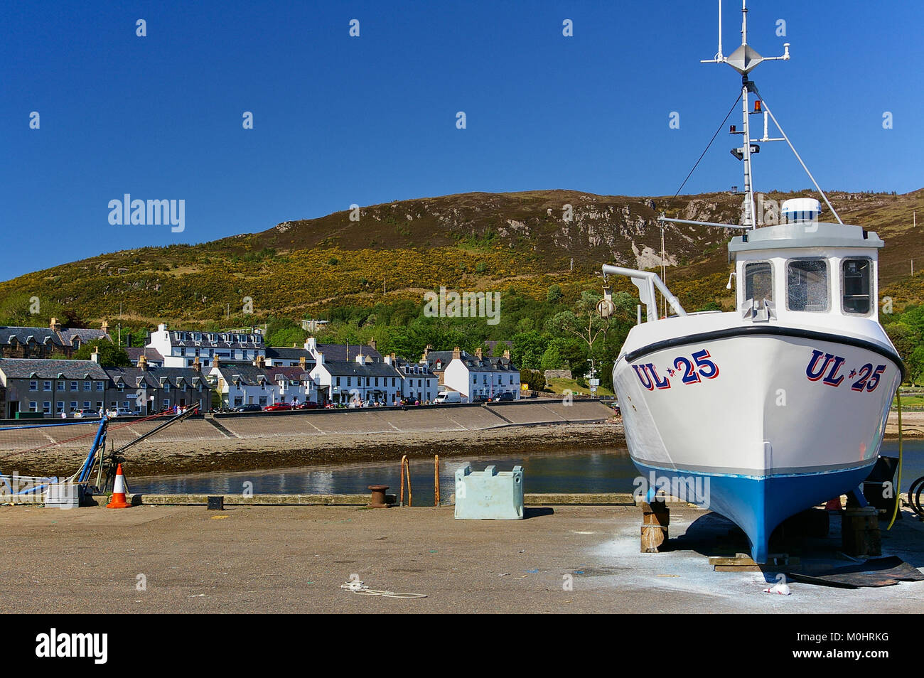 Ullapool, Scotland - May 27th, 2012 - White fishing boat ashore on the pier with harbor, picturesque waterfront buildings and mountain range in the ba Stock Photo