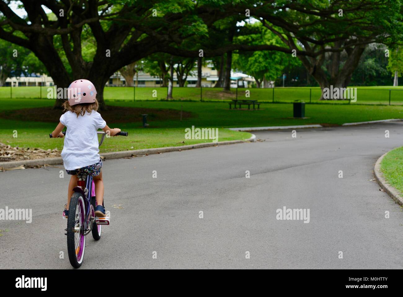 Young girl rides a bike on the road through Anderson Park Botanic