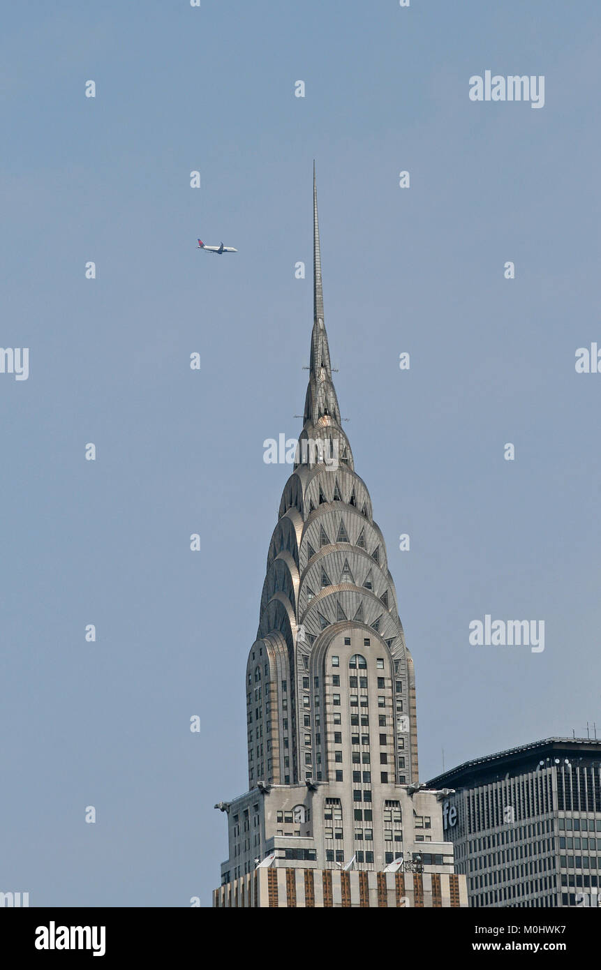 The tip of the Chrysler Building with a jet plane flying overhead, east side of Manhattan in the Turtle Bay area at the intersection of 42nd Street an Stock Photo