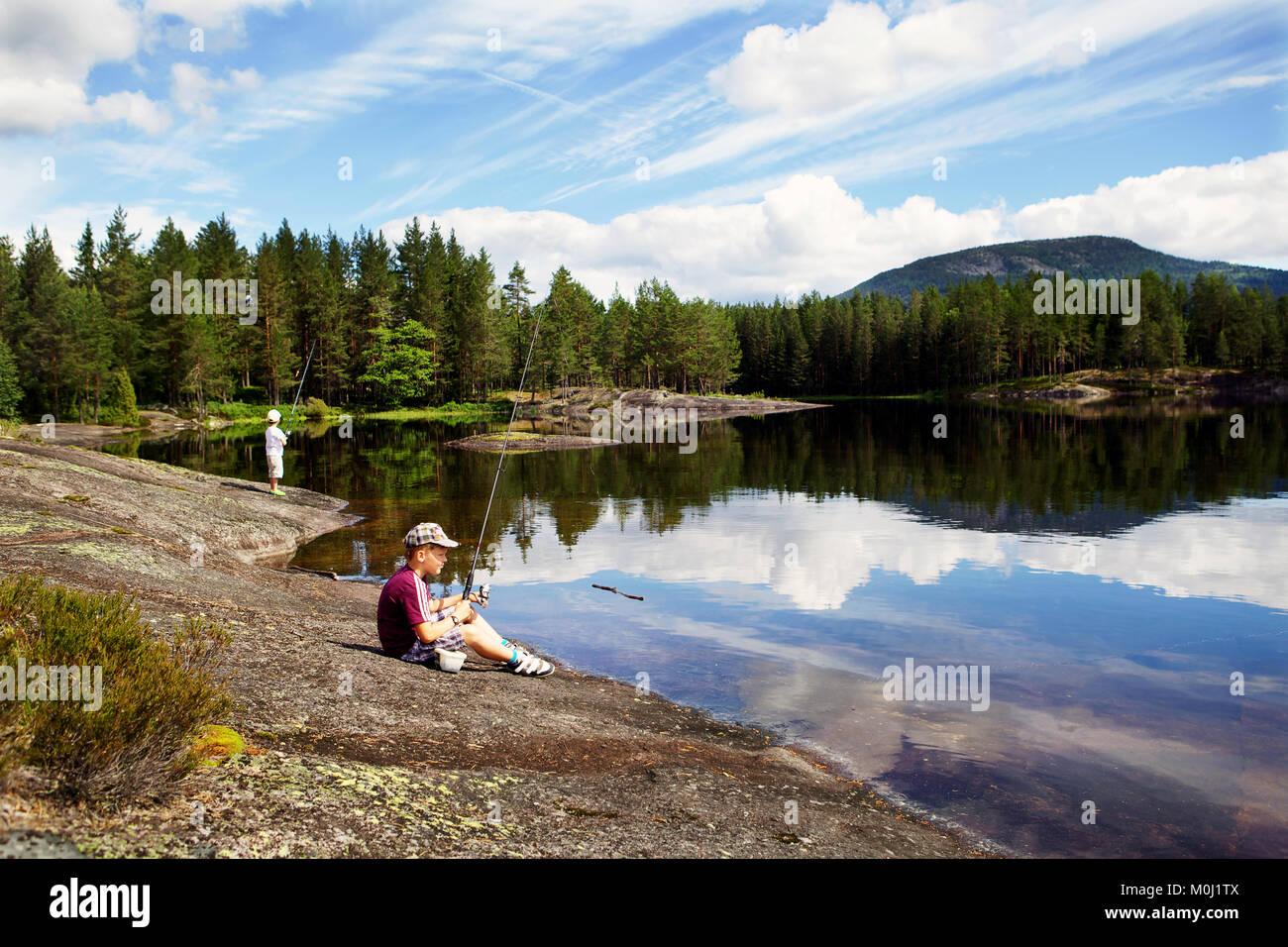 Two boys sitting on a scenic lake shore and fishing, Norway. Stock Photo