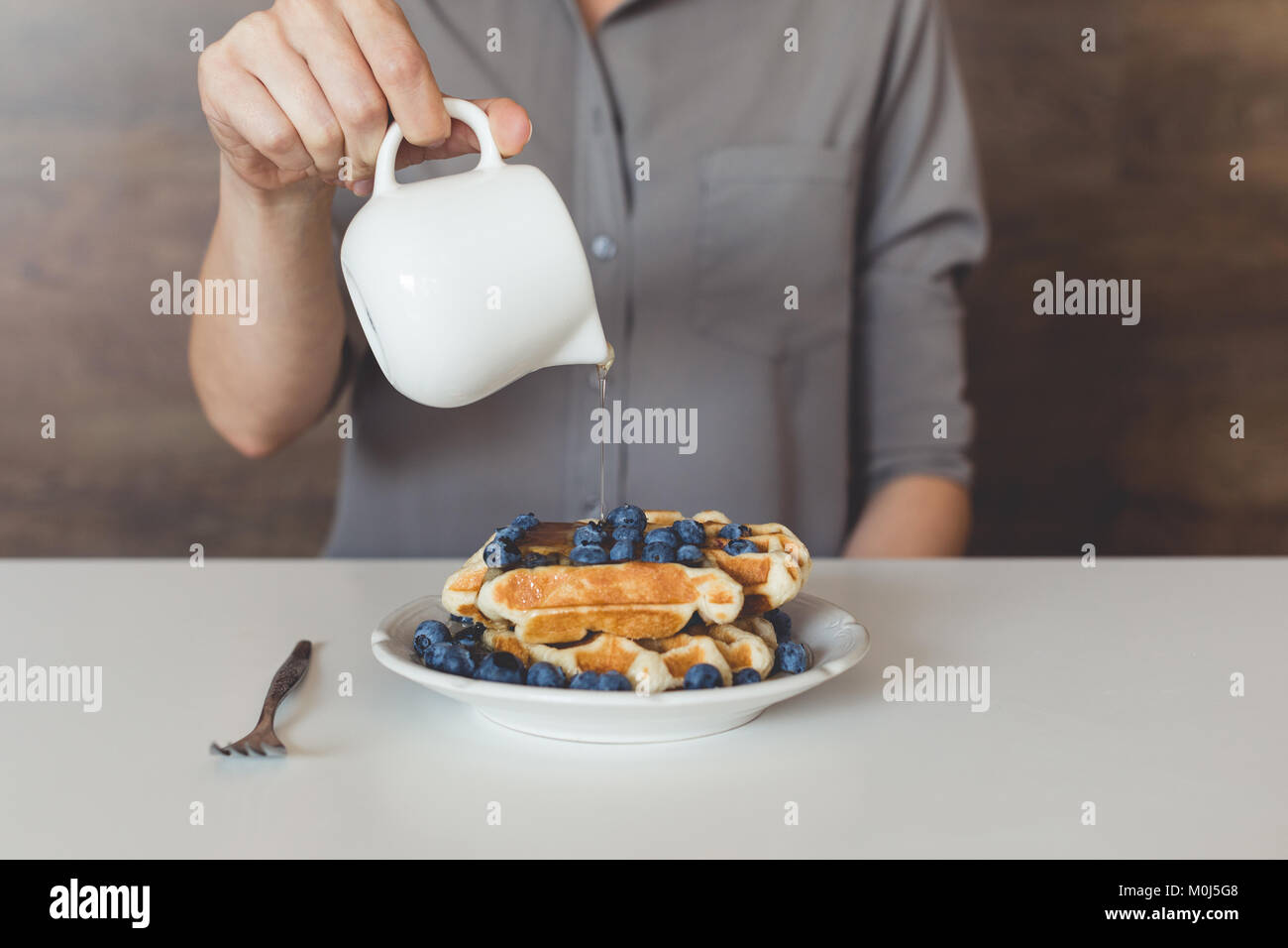 cropped shot of woman pouring sweet syrup on tasty waffles Stock Photo