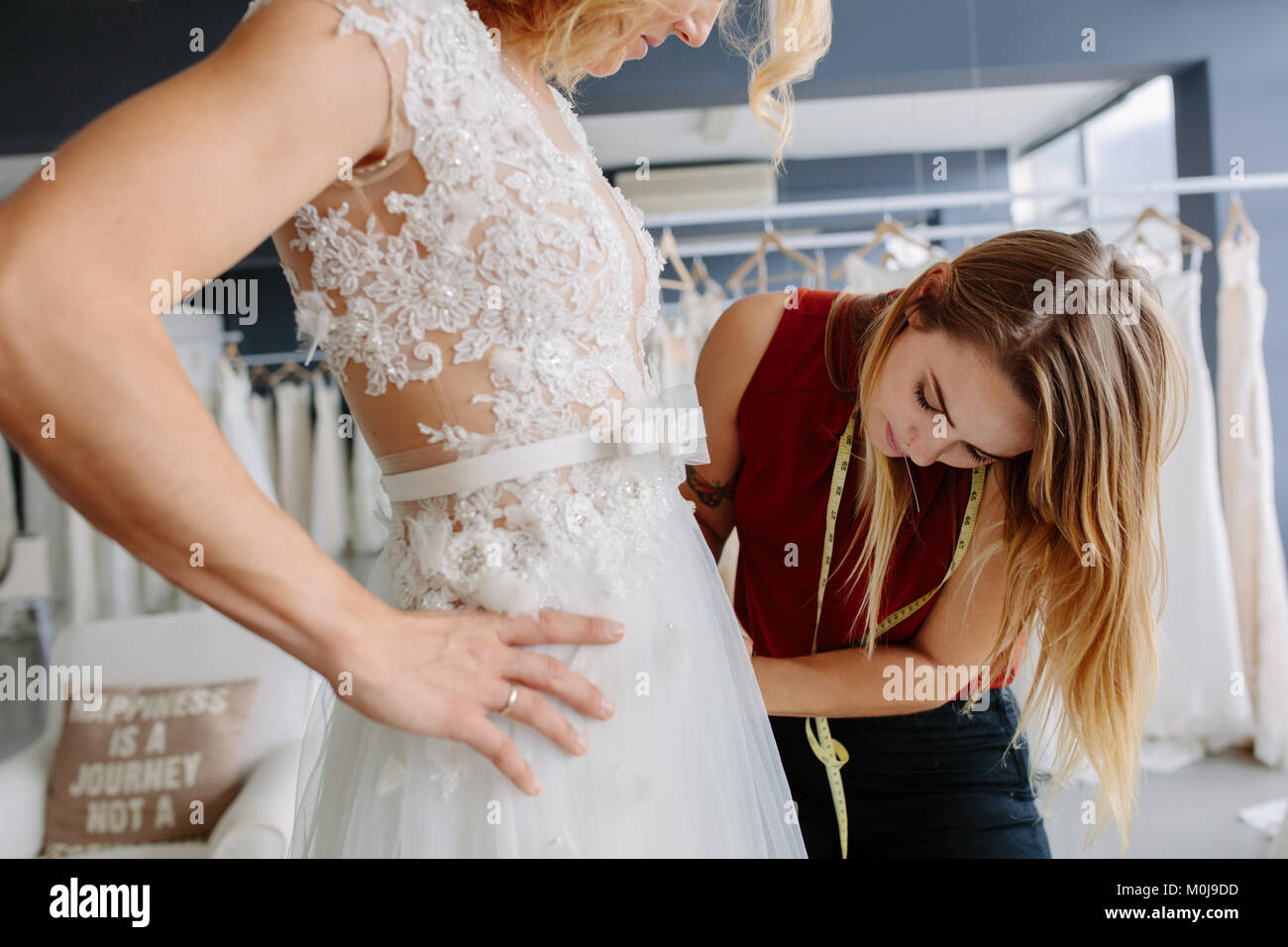 Skillful dress designer fitting wedding gown to woman in her boutique. Woman making adjustments to bridal gown in fashion designer studio. Stock Photo