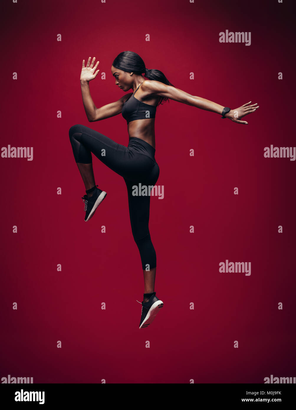 Sports woman doing jumping and stretching workout. Full length of healthy young african fitness woman doing exercise over red background. Stock Photo
