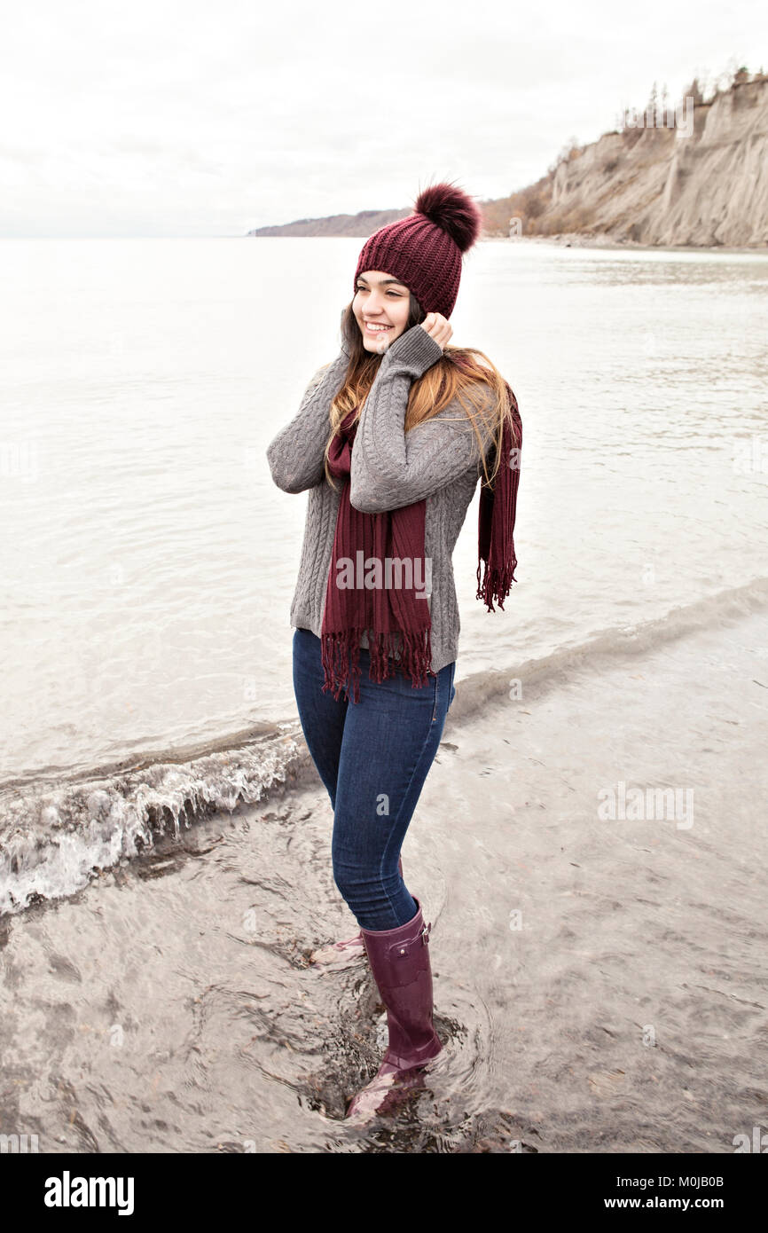 Girl standing in shallow water in autumn at the Scarborough Bluffs wearing a knit hat and scarf; Toronto, Ontario, Canada Stock Photo