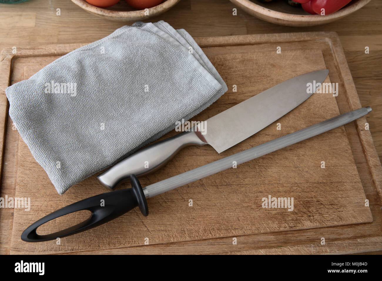 Chef's knife, honing steel and towel on cutting board, preparing for